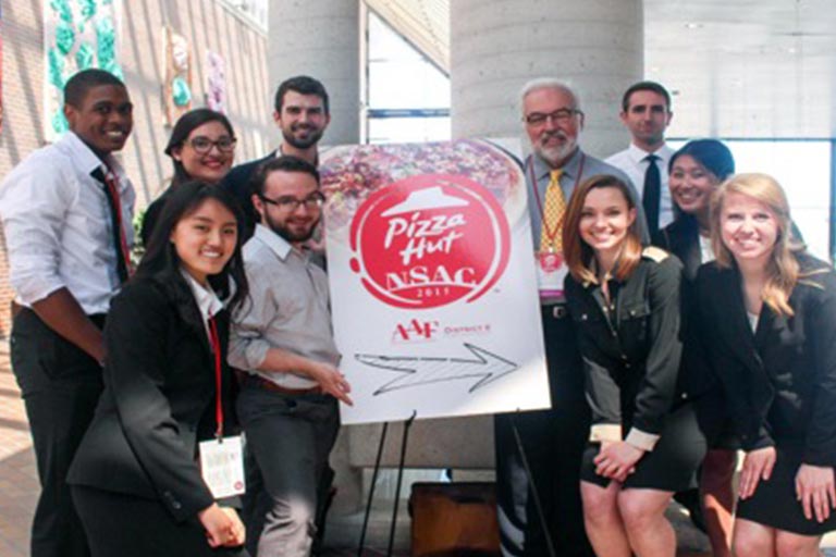 Bloomington Ad Club student members pose as a group with a Pizza Hut advertising poster.