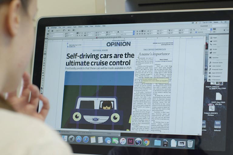 A student works on the layout of a news article using software and her laptop.