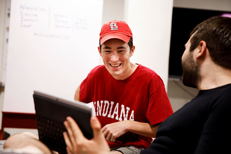 A student holds up a graphic drawing tablet for another student to see.