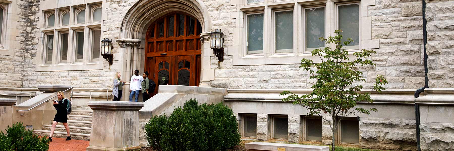 Students hang out and chat in front of Franklin Hall as a student walks out of the main entrance.