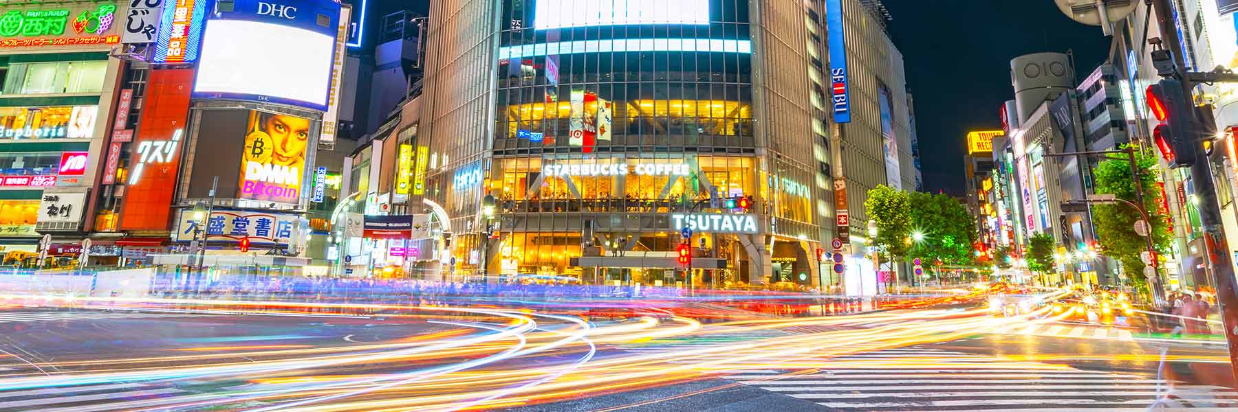 Buildings with brightly-lit advertisements at night with people and cars passing in front of them